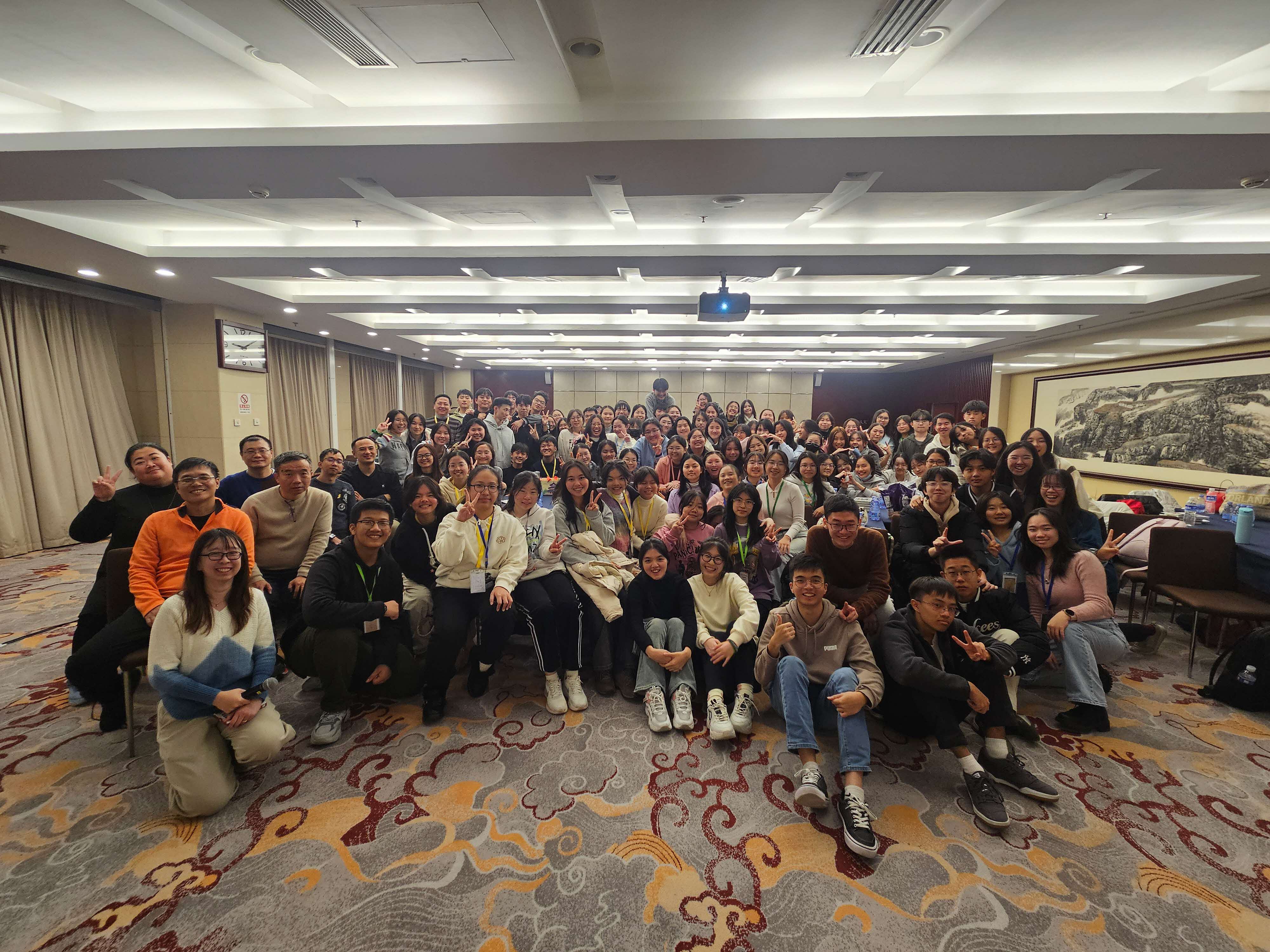A large of students and teachers taking a group photo in a hotel function room.